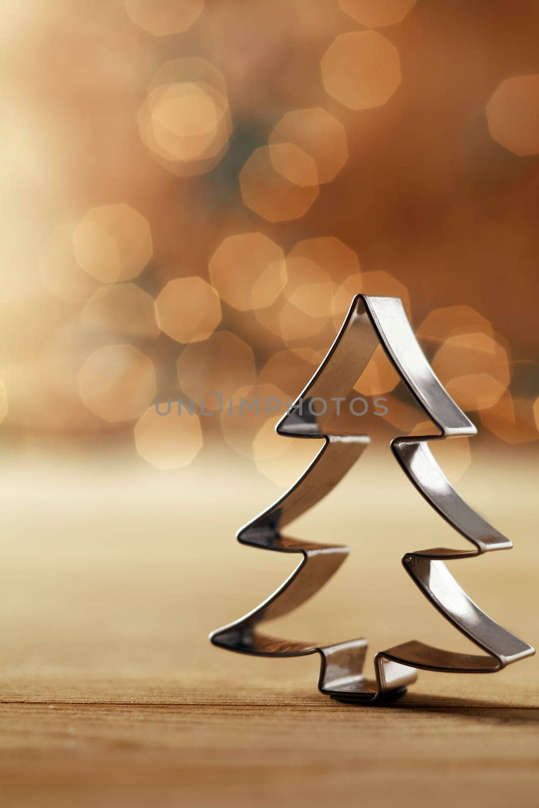 Shiny silver metallic Christmas tree cookie cutter decoration standing upright aginst a sepia background with a bokeh of sparkling party lights