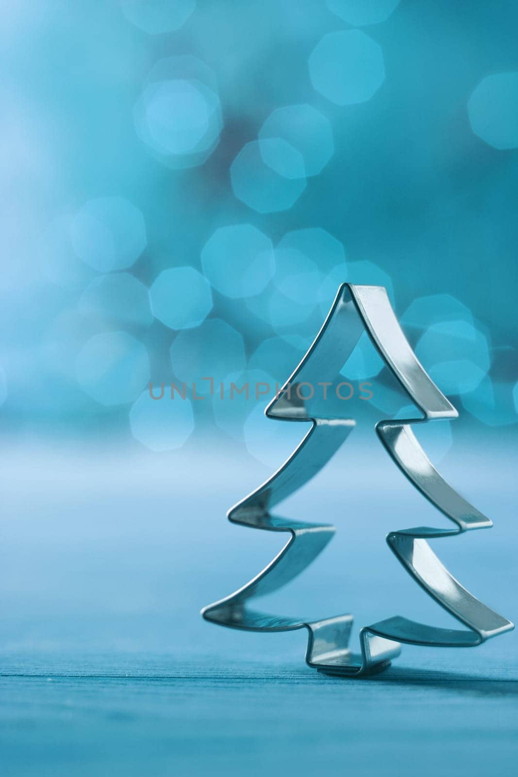 Christmas tree cookie cutter decoration on a cool winter blue background with a feint bokeh of party lights and copyspace for your Xmas greeting