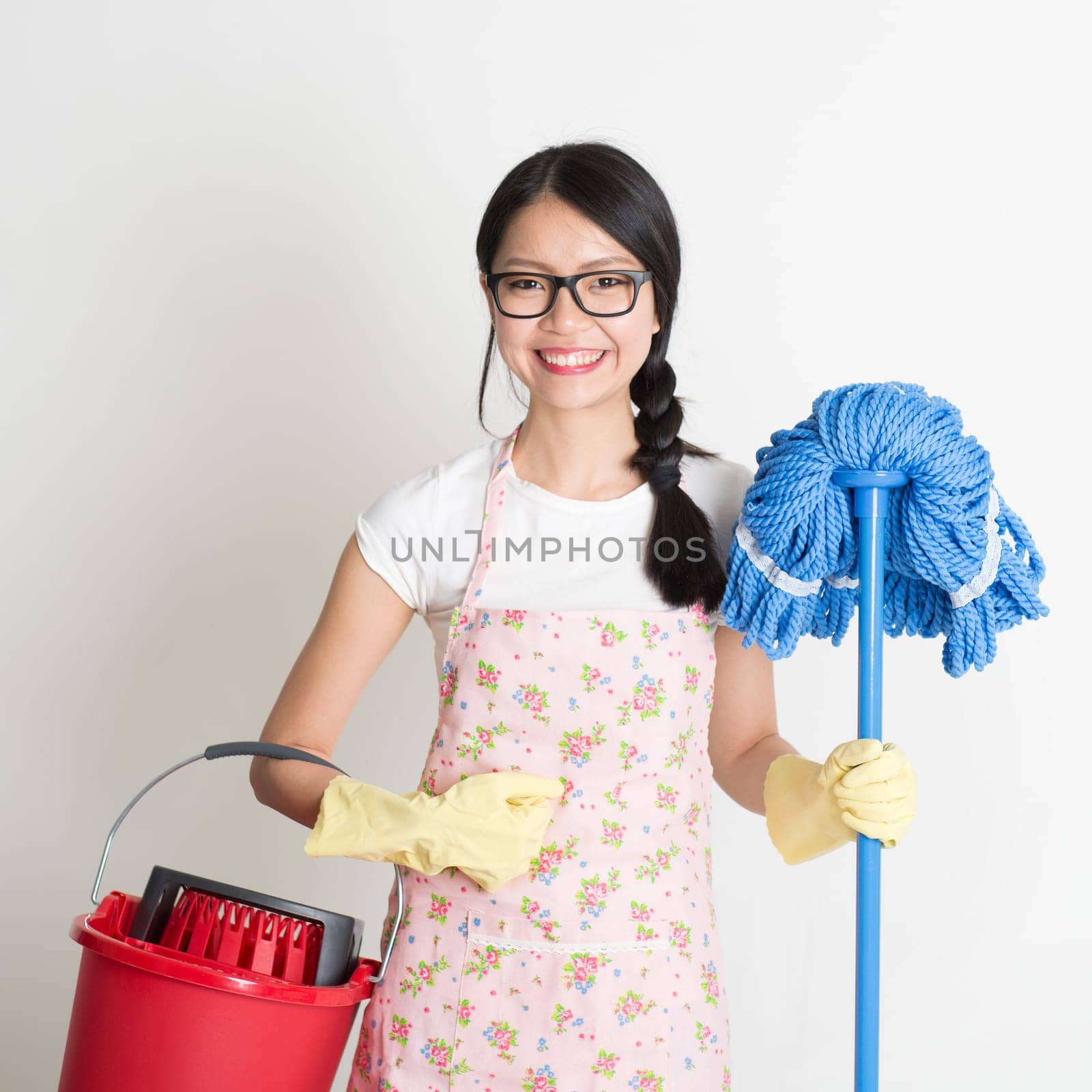 Portrait of Asian Chinese woman housekeeping, holding bucket and mop on plain background.