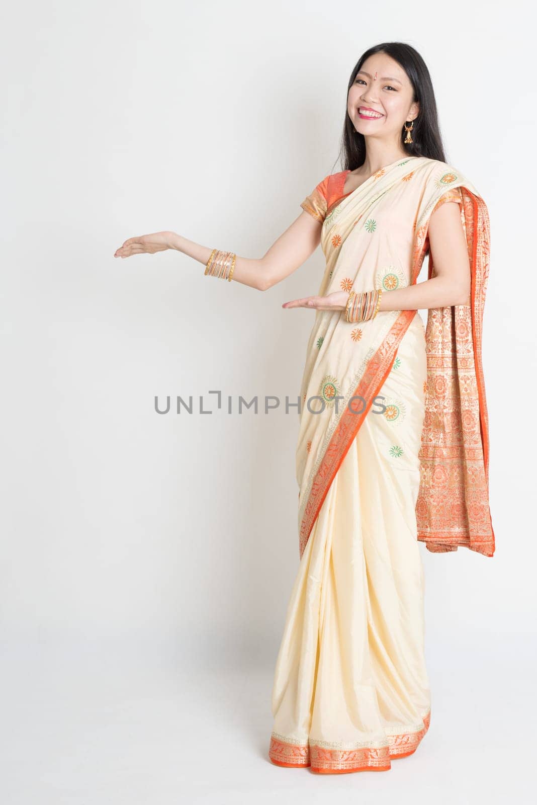 Full length Asian Indian girl hands showing something on plain background.