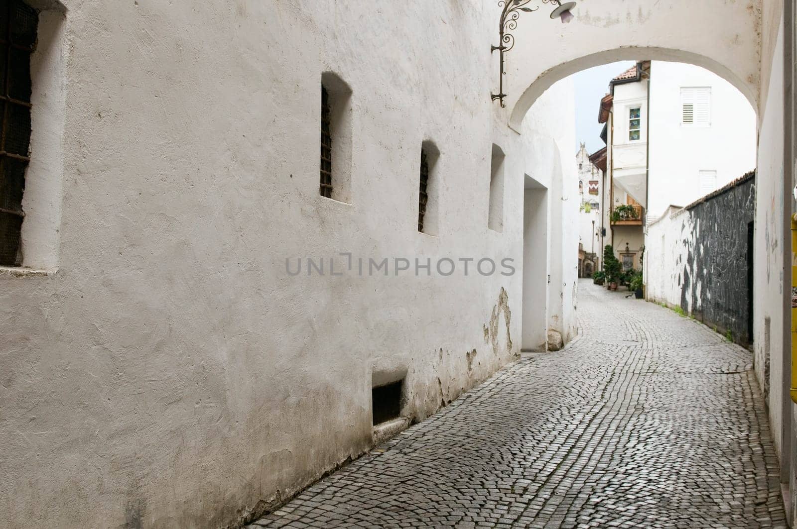 View into a small alley with arched element above and white plastered house walls and cobblestones in the city of Merano/South Tyrol