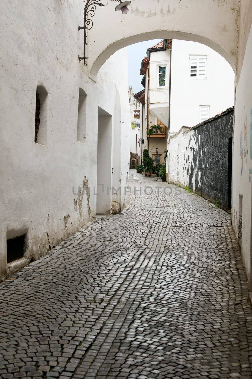 View into a small alley with arched element above and white plastered house walls and cobblestones in the city of Merano/South Tyrol
