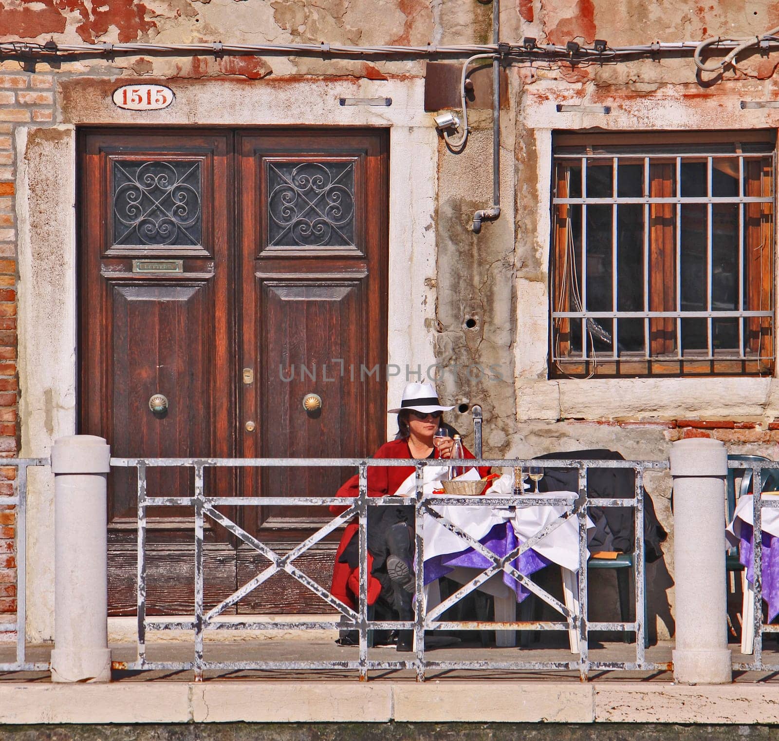 Every day life in Venice, woman with straw hat seats outside and drinks leisurely a glass of white wine