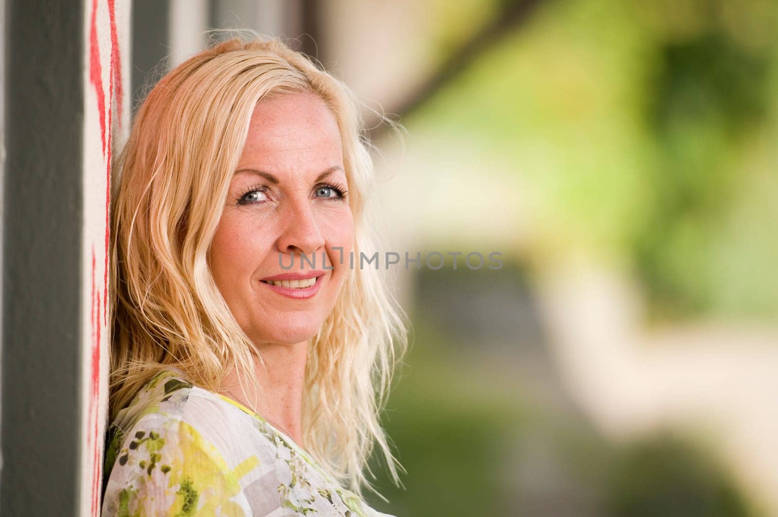 Side head portrait of a middle-aged blonde woman with her back standing on a painted wall and looking into the camera