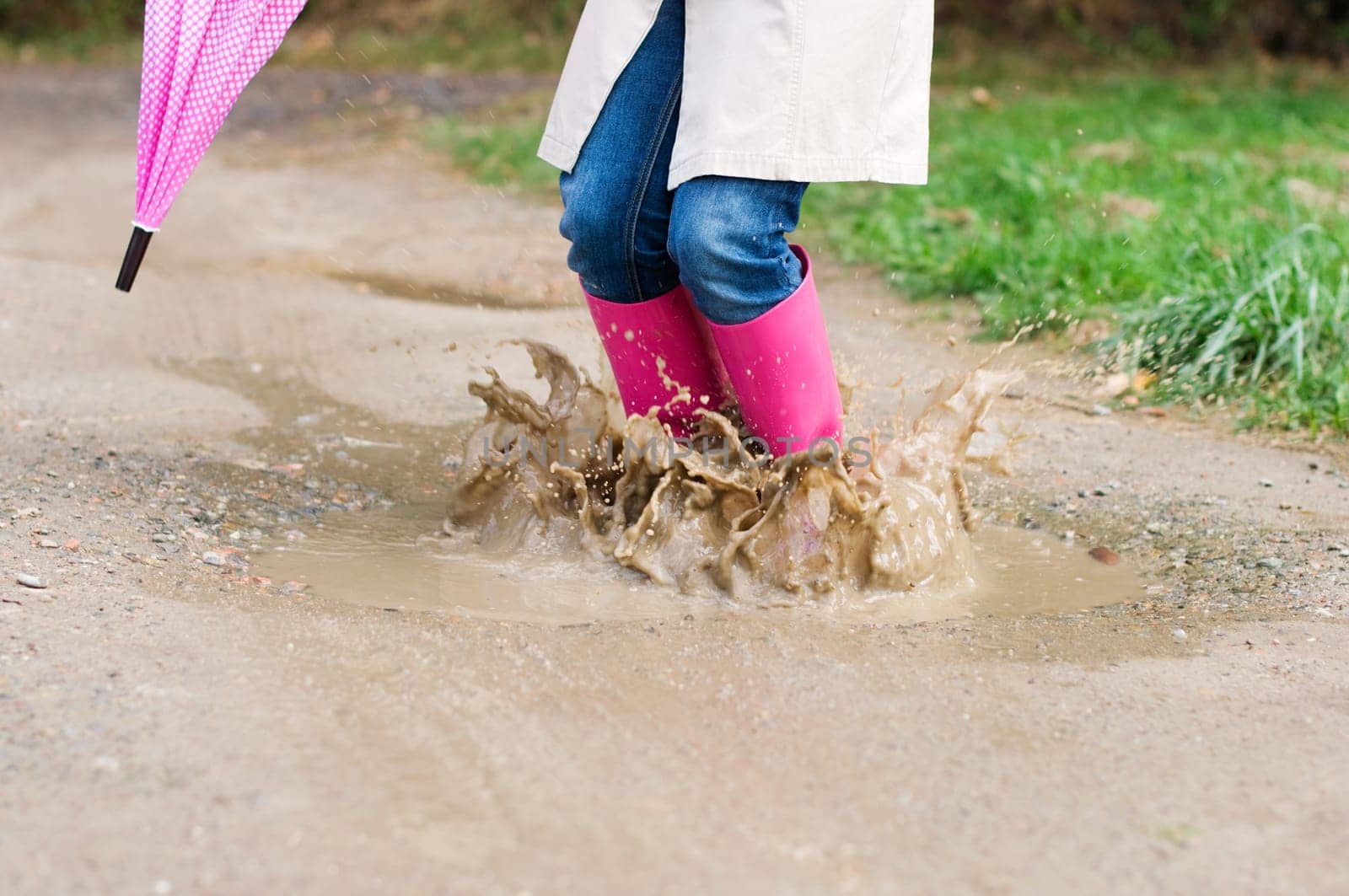 Young woman with rubber boots jumping in puddle
