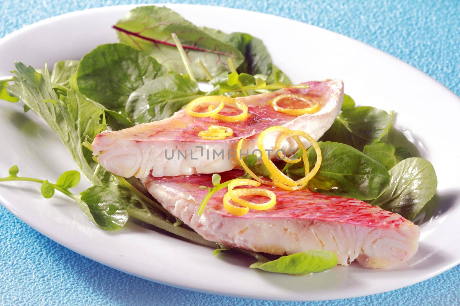Grilled fresh fish fillets garnished with lemon zest on leafy green salad with herbs and baby spinach for a tasty seafood meal or appetizer