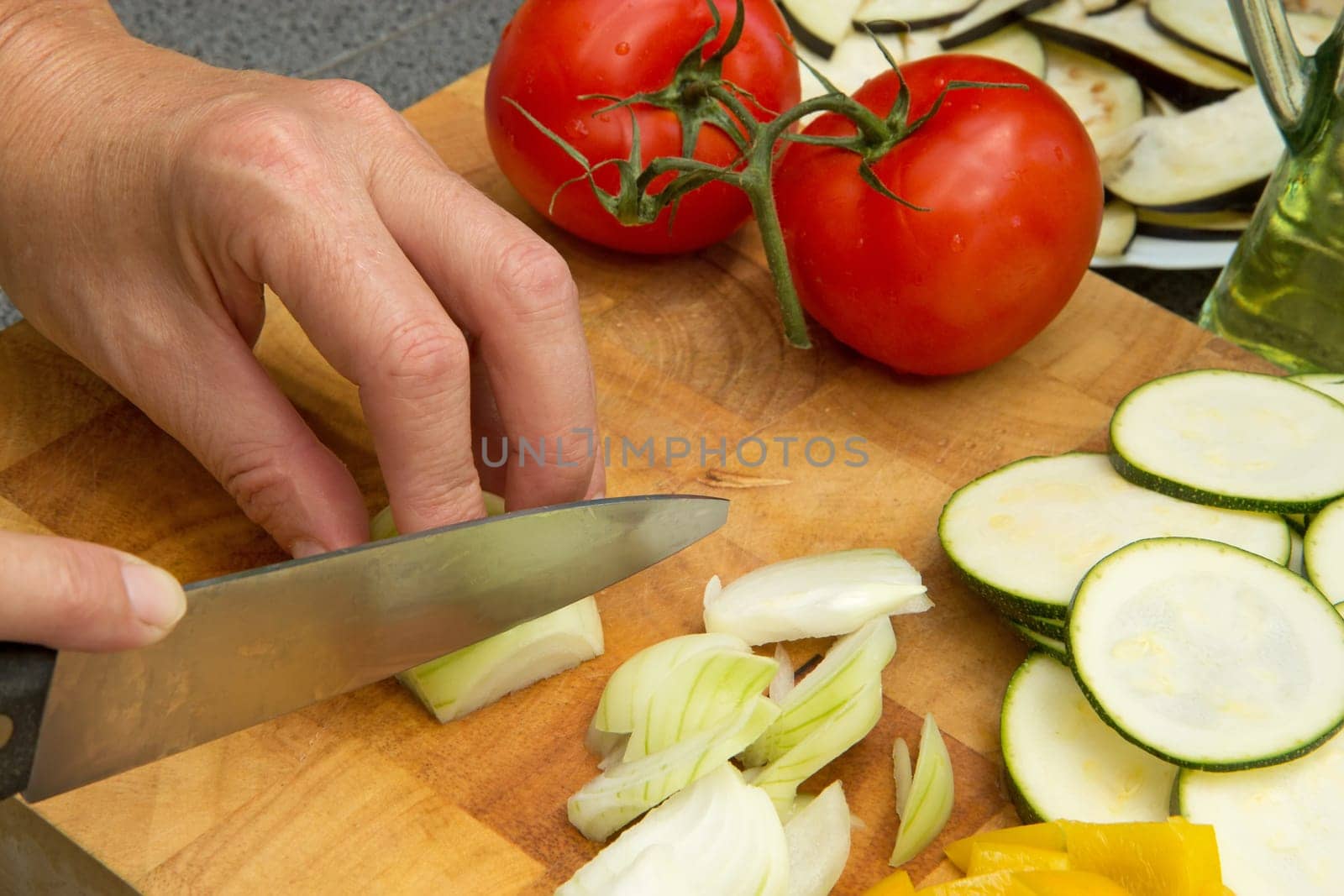 Woman's hand is slicing the onion  on a wooden board.