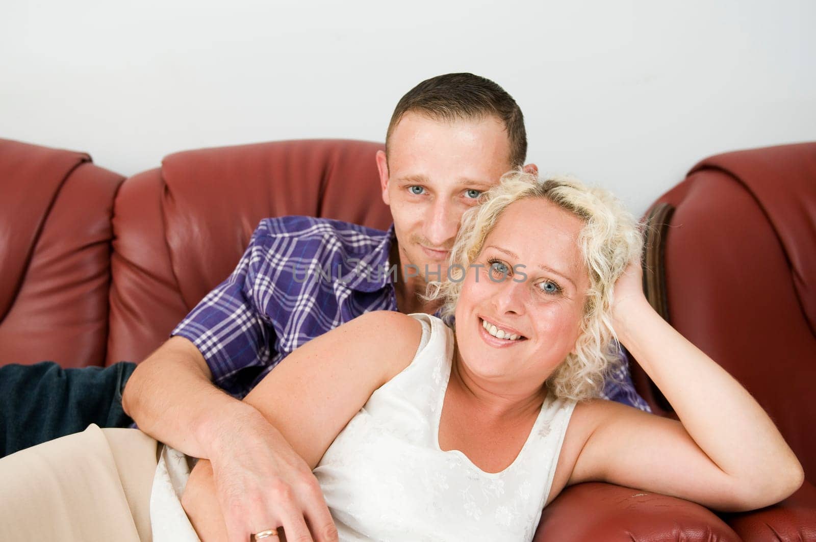 Torso portrait of a young couple lying on a brown leather sofa and happily smiling into the camera