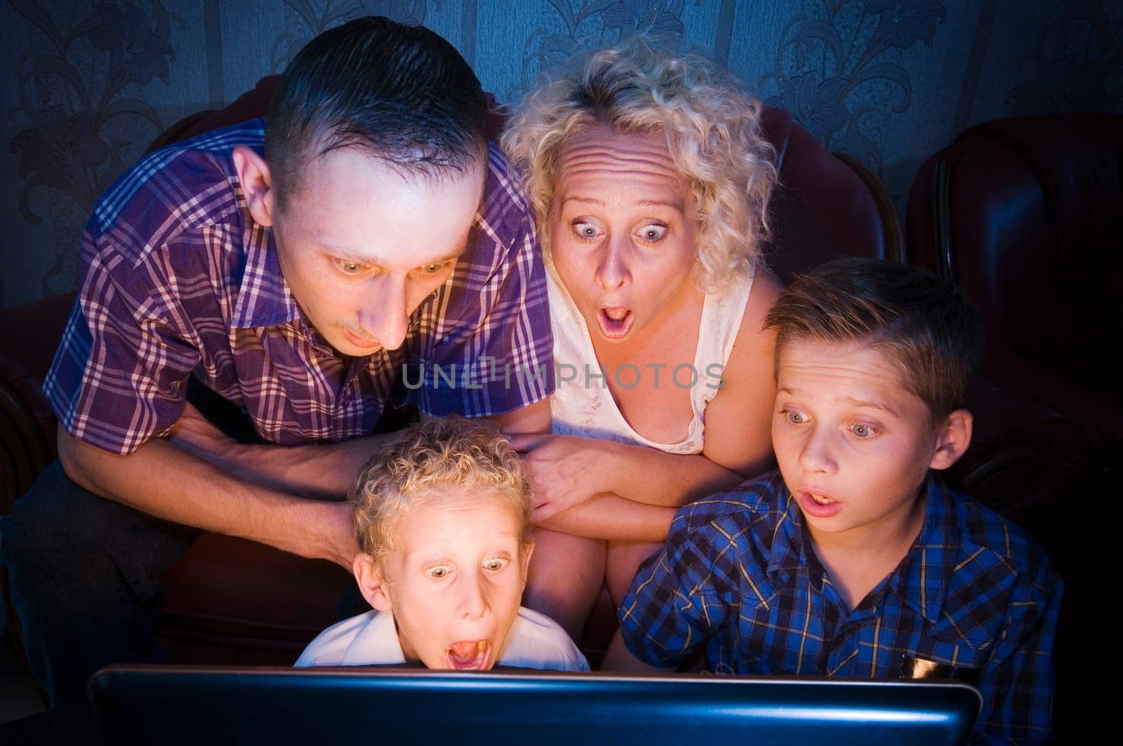Parents with their two sons,aged 7 and 13,sitting on the couch in a darkened room and looking at the camera in shock at a monitor
