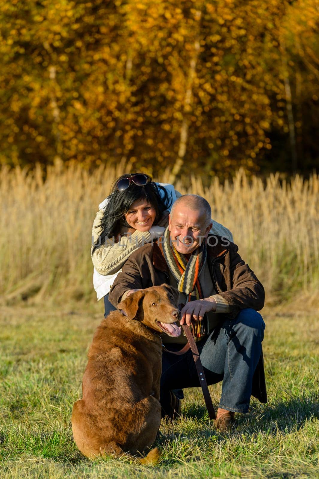Cheerful couple with retriever dog in autumn countryside sunset