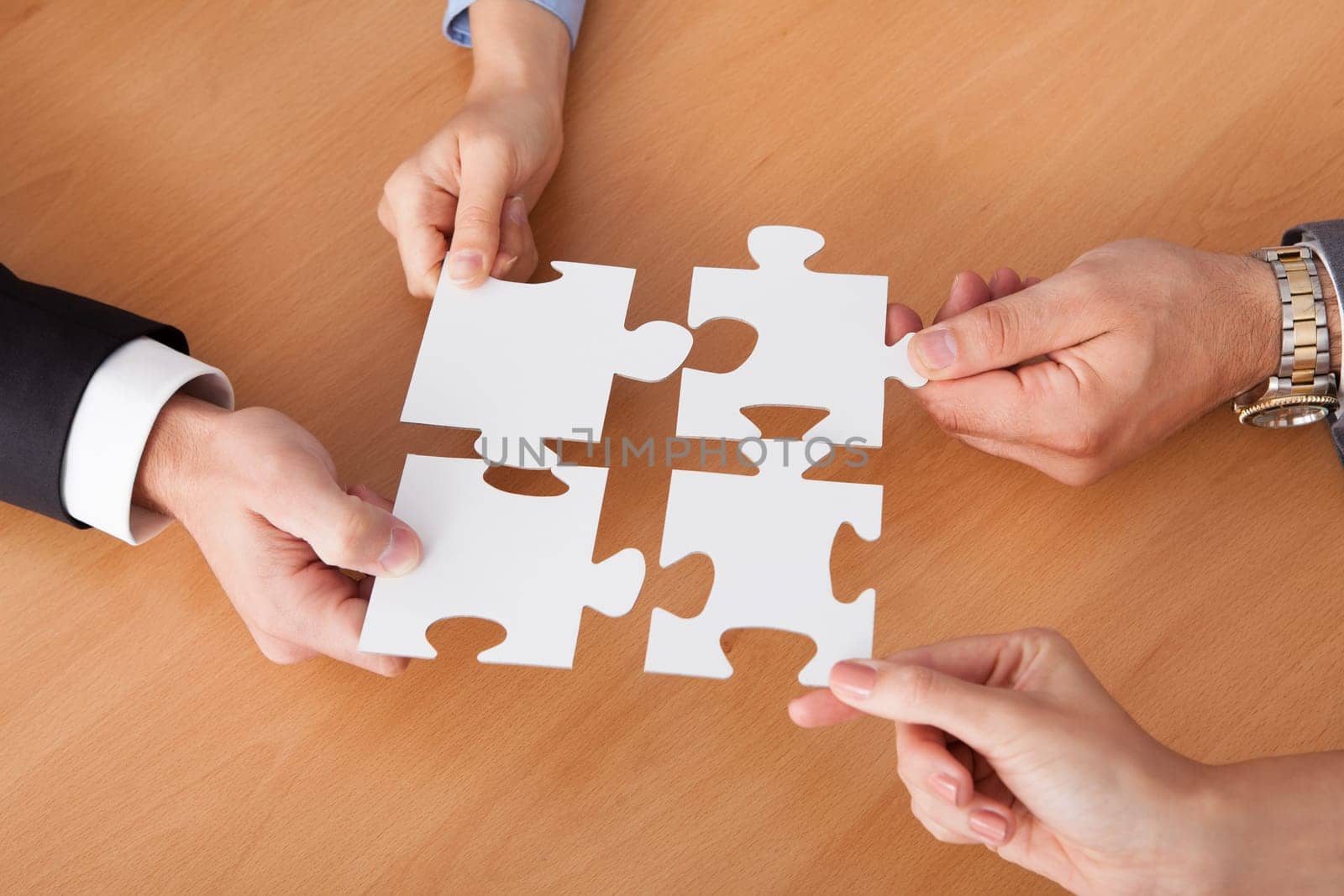 Close-up Of Businesspeople Holding Jigsaw Puzzle Over Desk