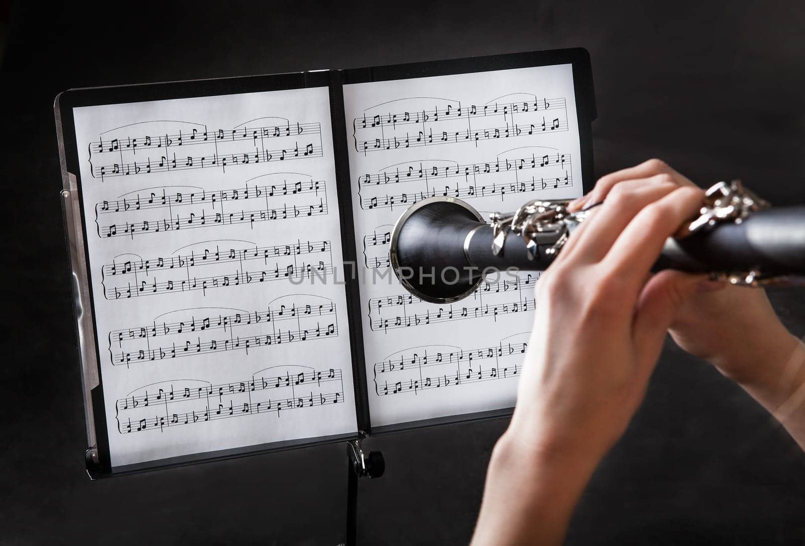 Beautiful young woman playing clarinet over black background