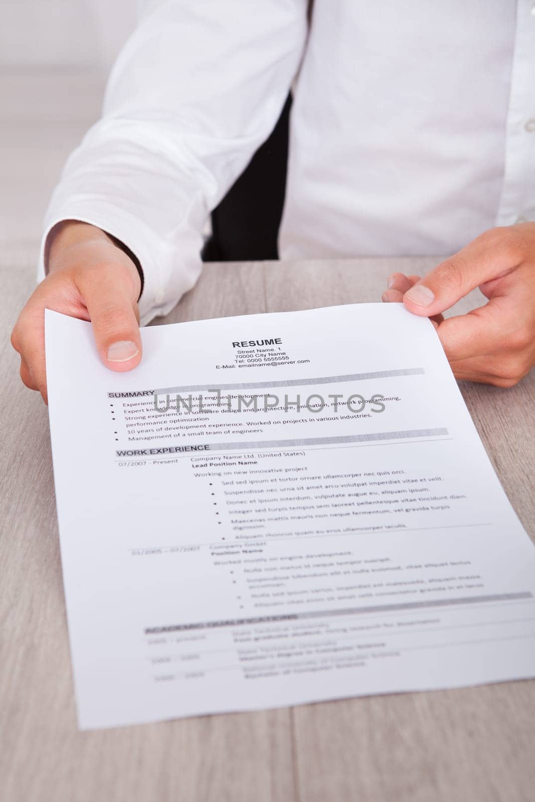 Close-up Of Businessman's Hand Holding Resume On Desk