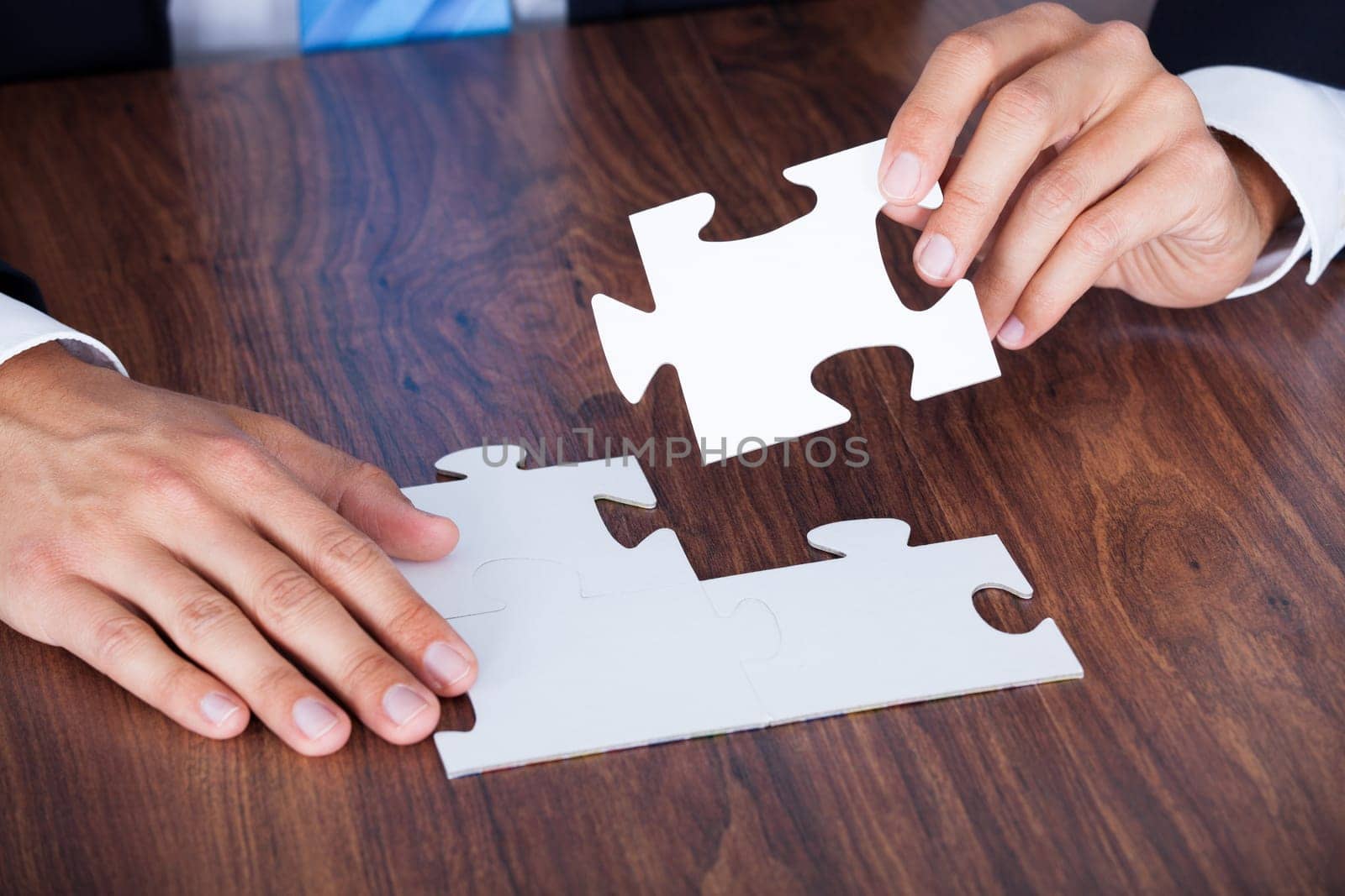 Close-up Of Businessman Hands Completing Jigsaw Puzzle