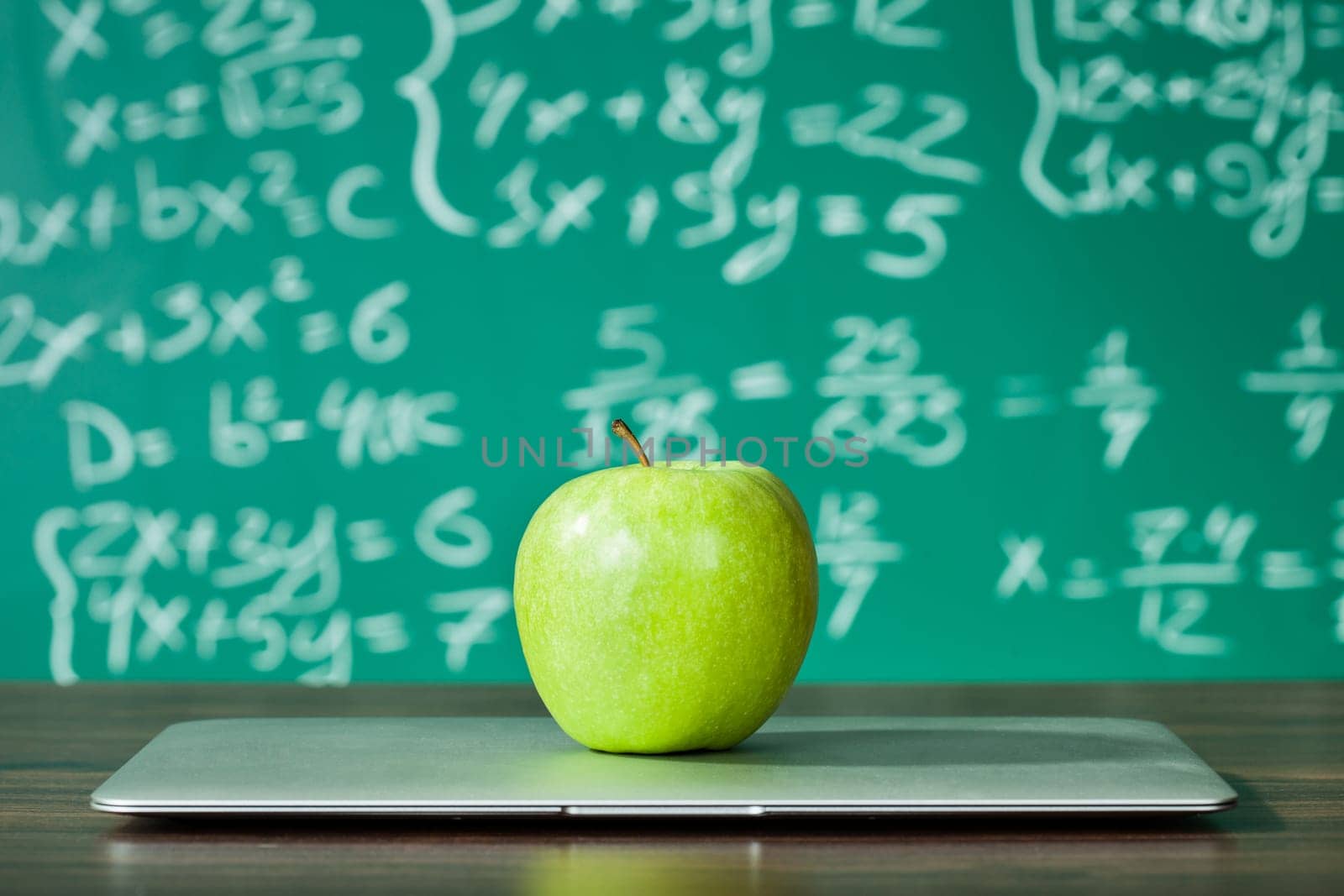 Laptop and apple on the desk in front of blackboard