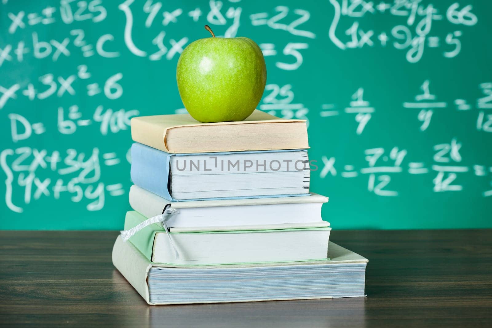 Stack of school textbooks and apple in front of blackboard