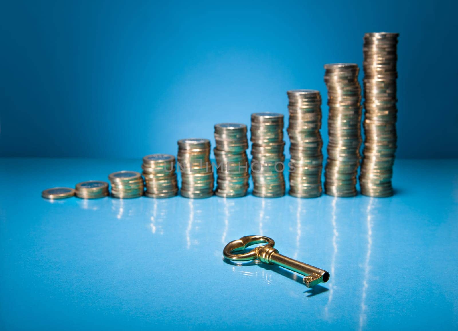 Stack Of Golden Coin And Key Over Blue Background