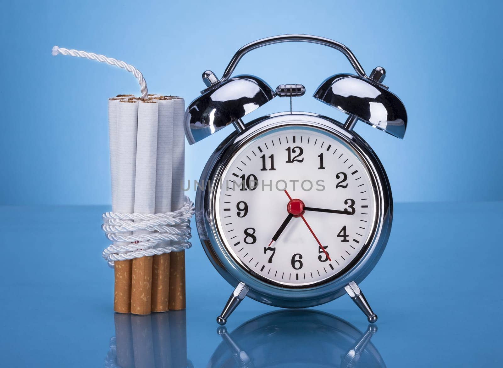 Cigarettes Tied With Rope And Alarm Clock Over Blue Background