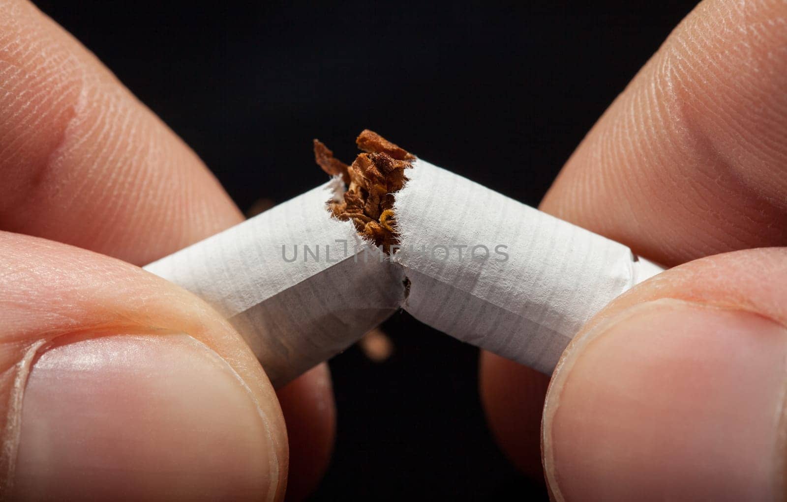 Close-up Of  Hand Breaking Cigarette Over Black Background