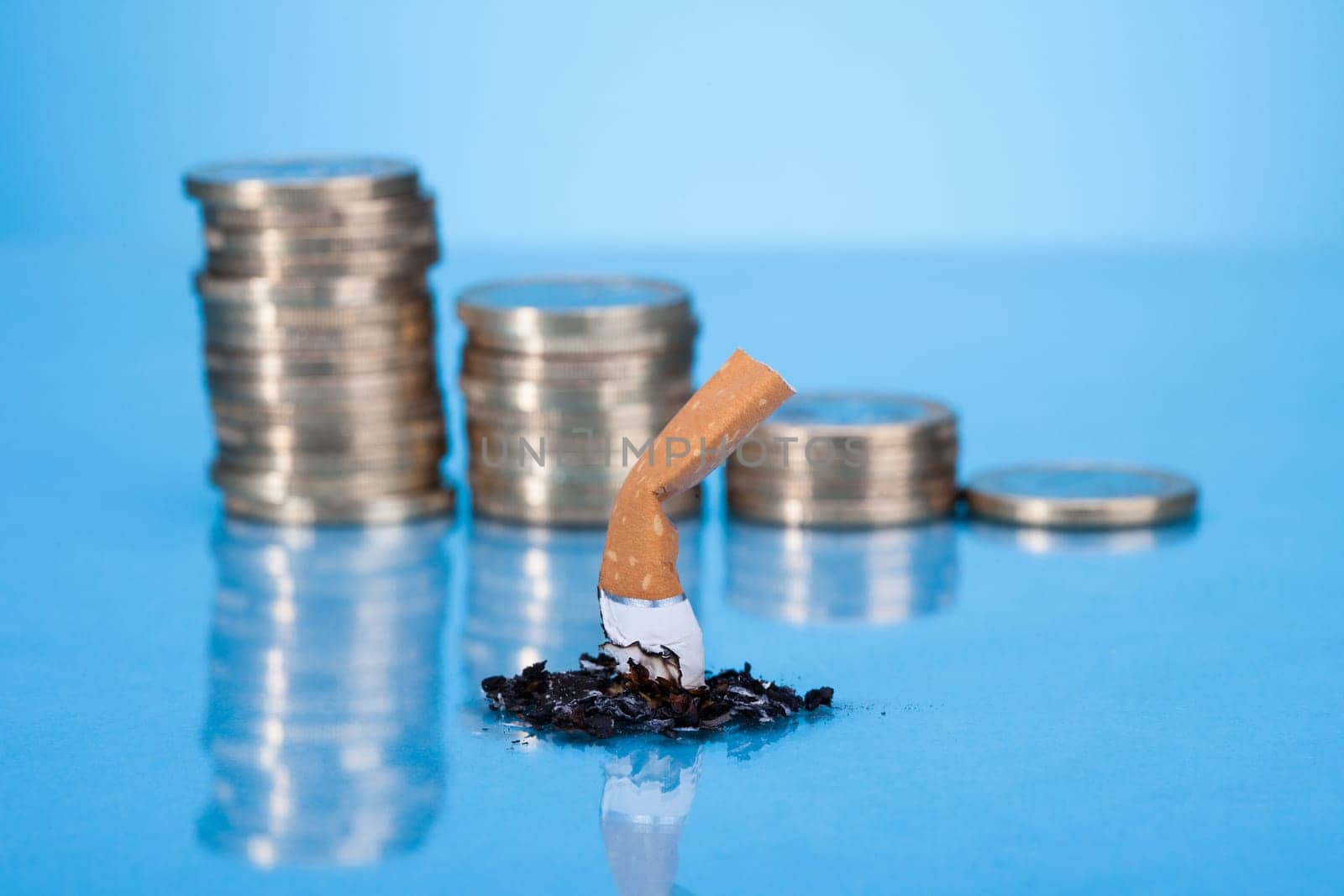 Single Cigarette Butt With Ash And Coin Stack On Blue Background