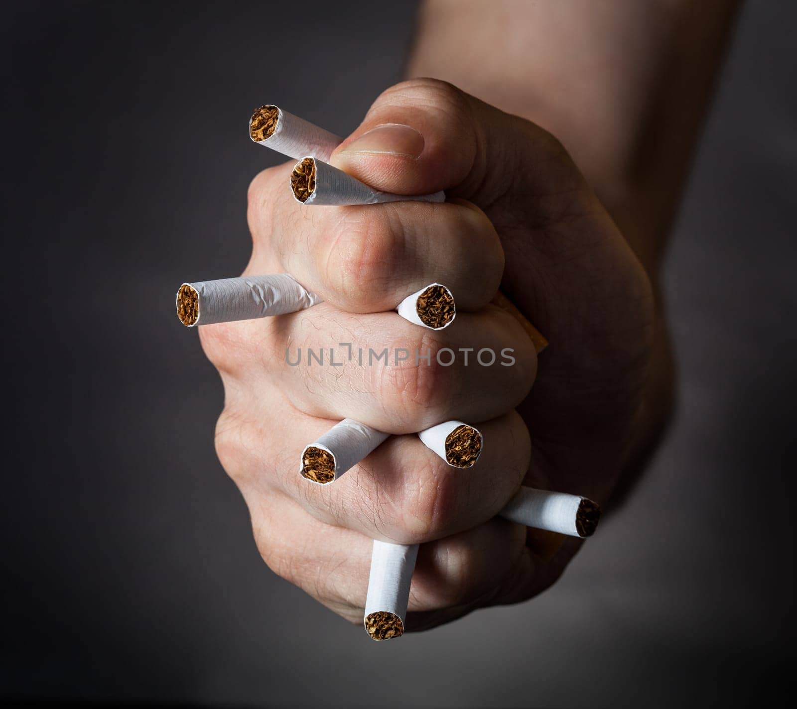 Male Fist Piercing Cigarettes Over Black Background