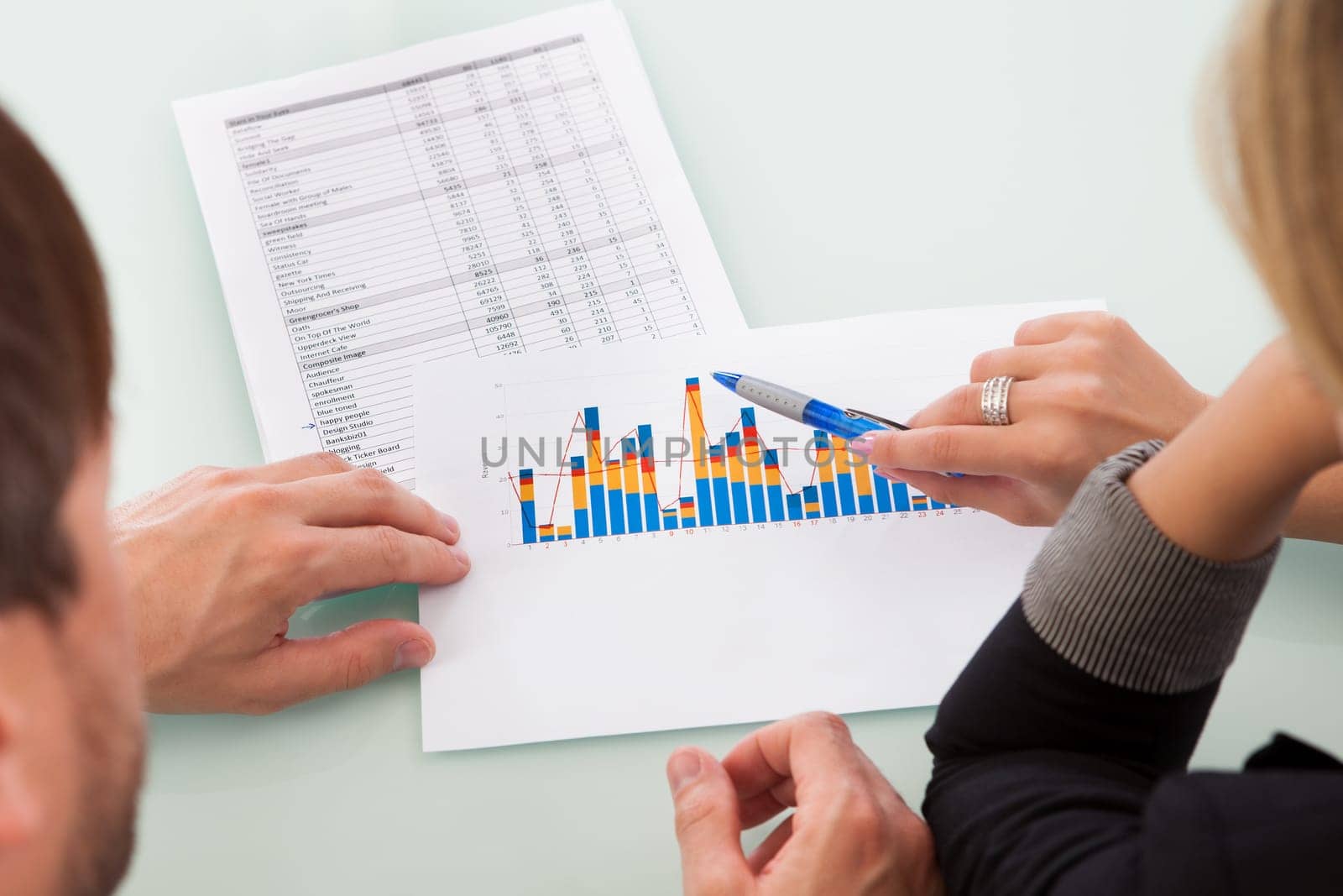 Over the shoulder view of two business partners discussing a colorful fluctuating bar graph comparing it with a text table