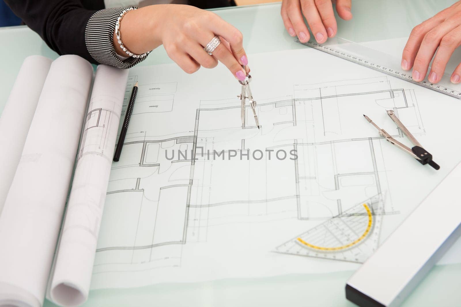 Cropped overhead view of a male and female architect discussing a set of blueprints spread out on a table