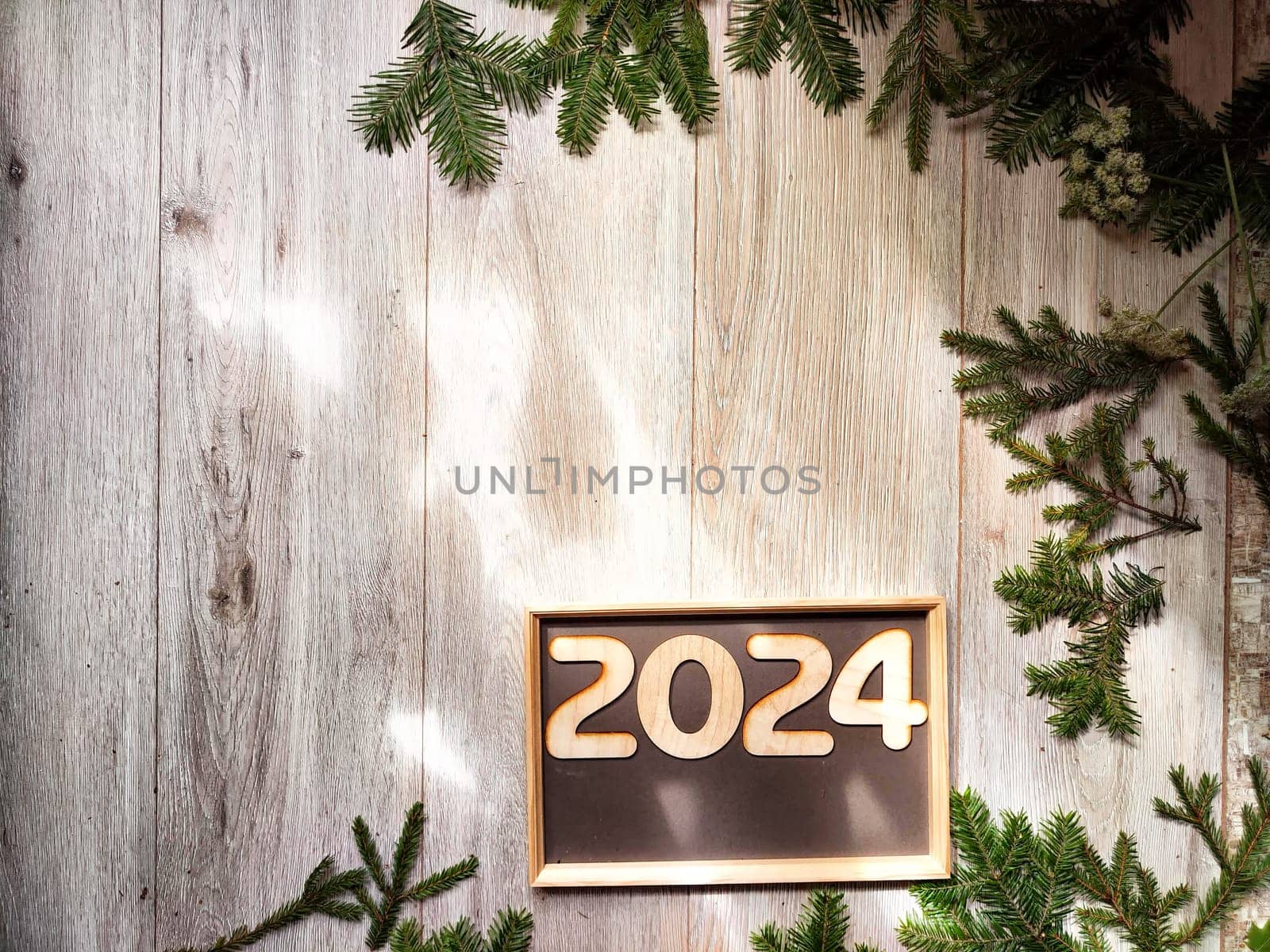 Wooden figures and numbers of the new year 2024 with frame and fir branches of Christmas tree. Celebration. Abstract background, pattern, frame, place for text, copy space