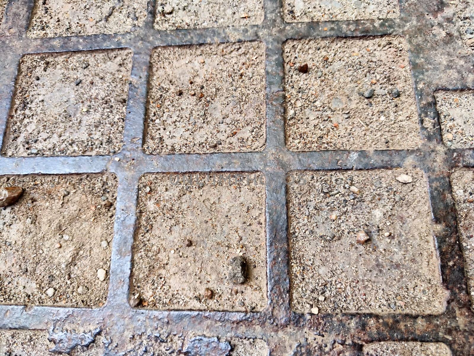 Squares in a metal grid lying on concrete, pebbles, earth. The old sidewalk or wall. Pattern of metal rods. Background, texture, frame, copy space