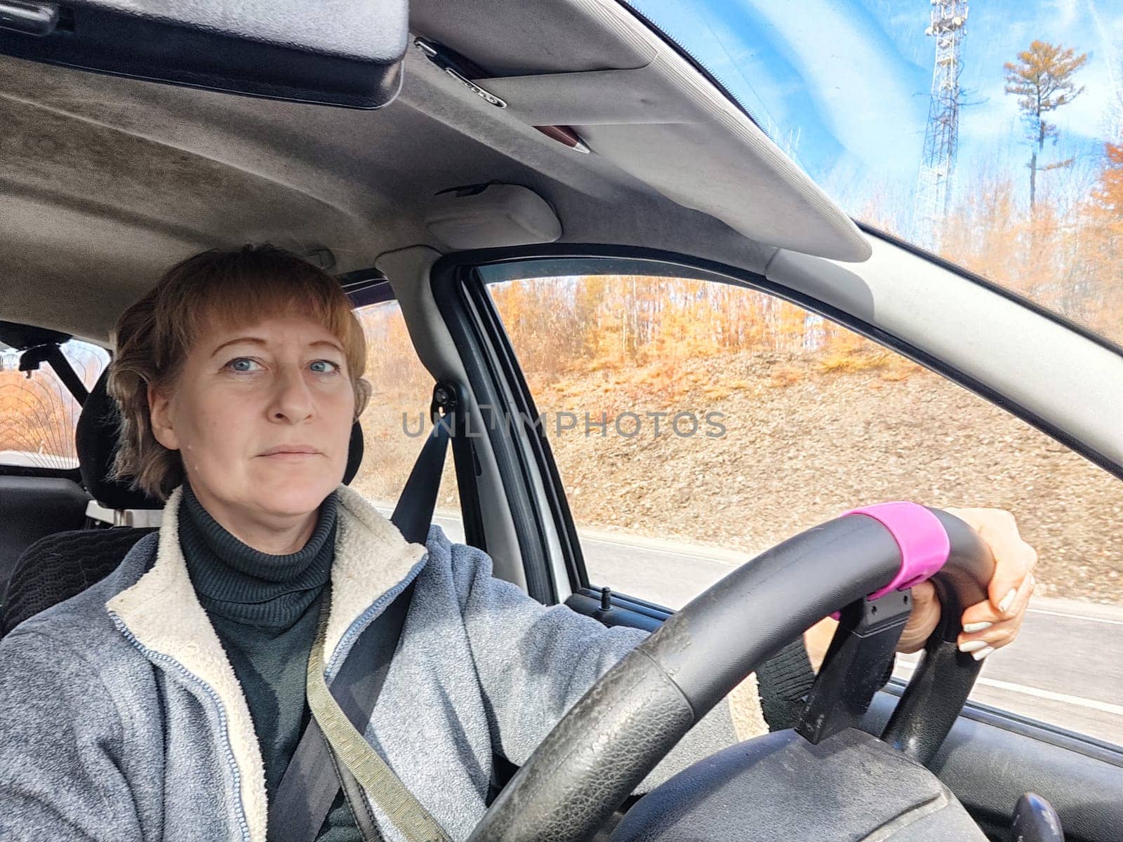 Portrait of female driver in solo journey. Adult mature woman holding steering wheel and looking through windscreen in travel by vehicle on vacation. Lady girl who is owner or rent car for travel