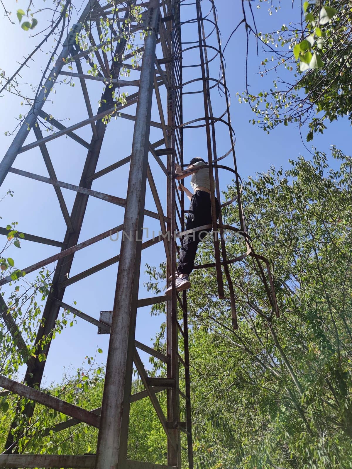 teenage girl climbing without a safety net onto an abandoned rusty metal tower,