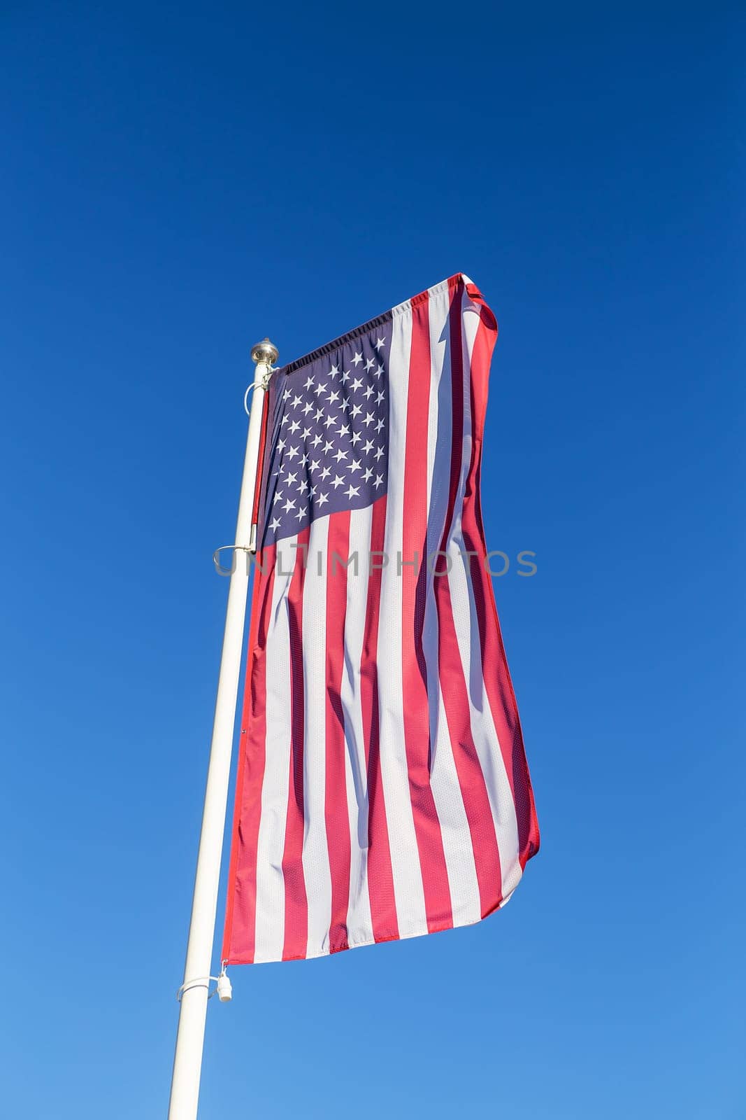 The American flag flies against a clear blue sky, vertical. Freedom and independence concept. The national flag is one of the symbols of the state