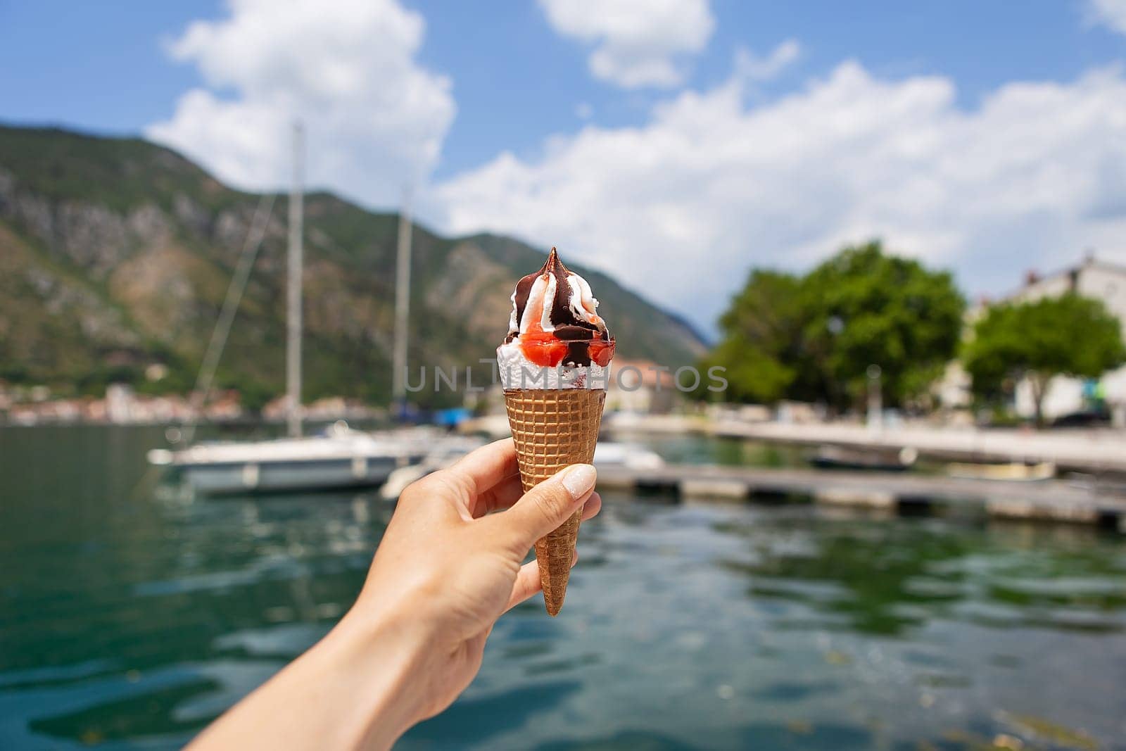 Very beautiful embankment of the Bay of Kotor, Montenegro. A girl holds colorful ice cream on the background of the Bay of Kotor. by sfinks