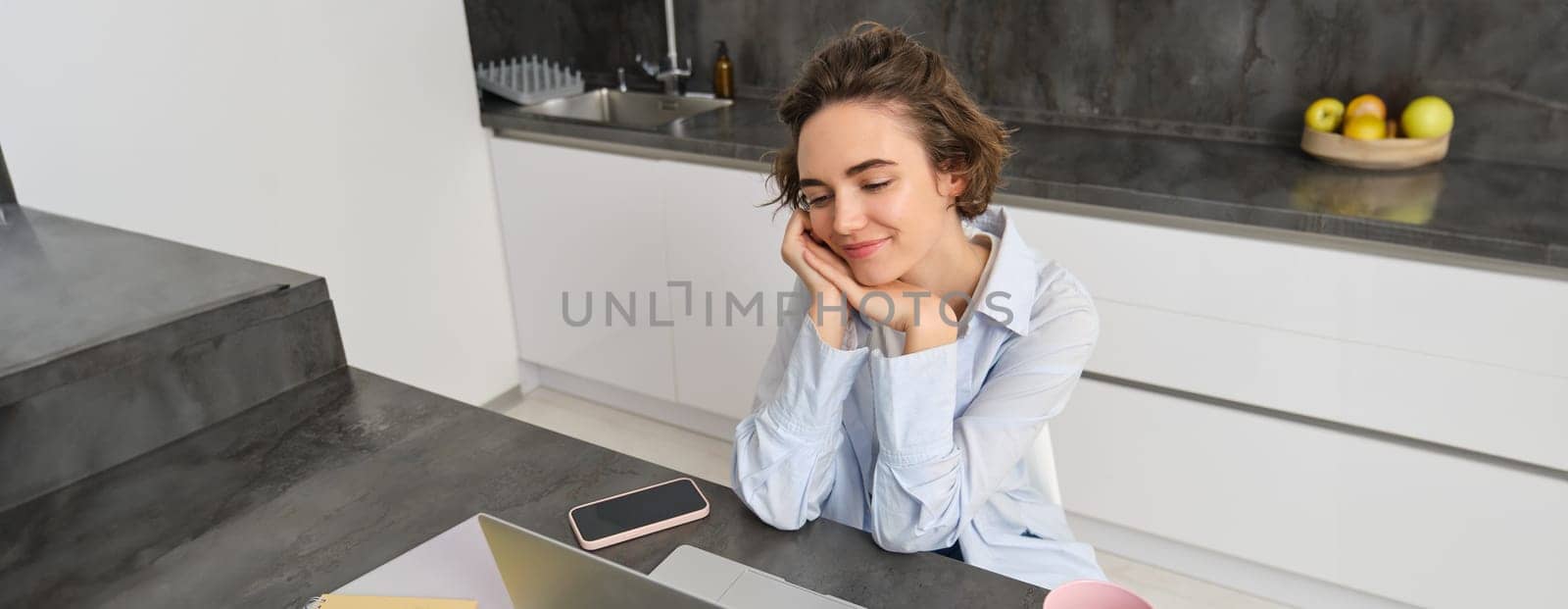 Portrait of beautiful girl student, doing online course from home, studying on laptop, looking at screen and smiling by Benzoix