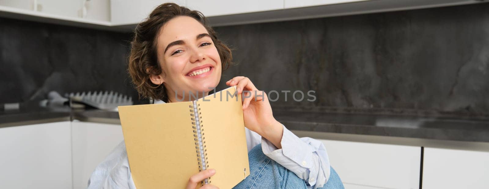 Happy young woman studying at home, reading journal, preparing for exam, looking at her notes in notebook by Benzoix