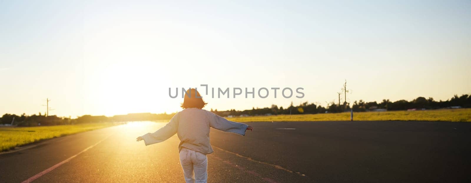 Rear view photo of young girl riding skateboard towards sunlight. Happy young woman on her cruiser, skating on longboard.