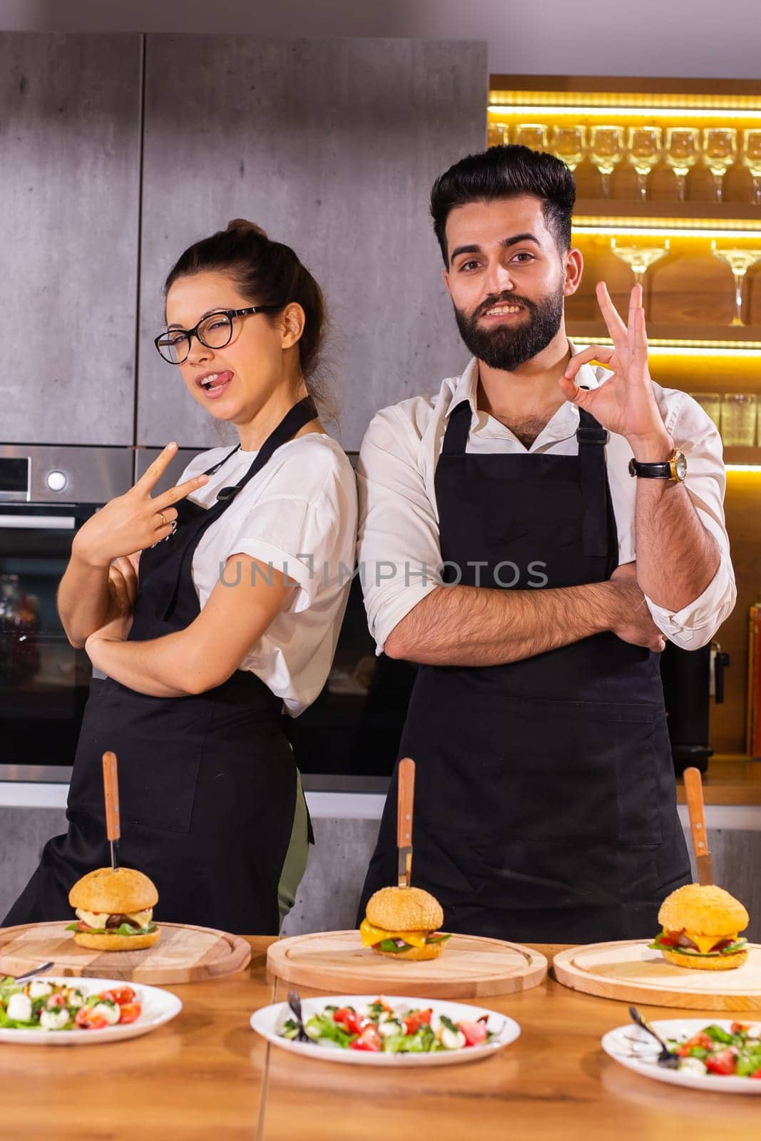 Happy chef and his colleague standing at kitchen and looking at camera - food and restaurant