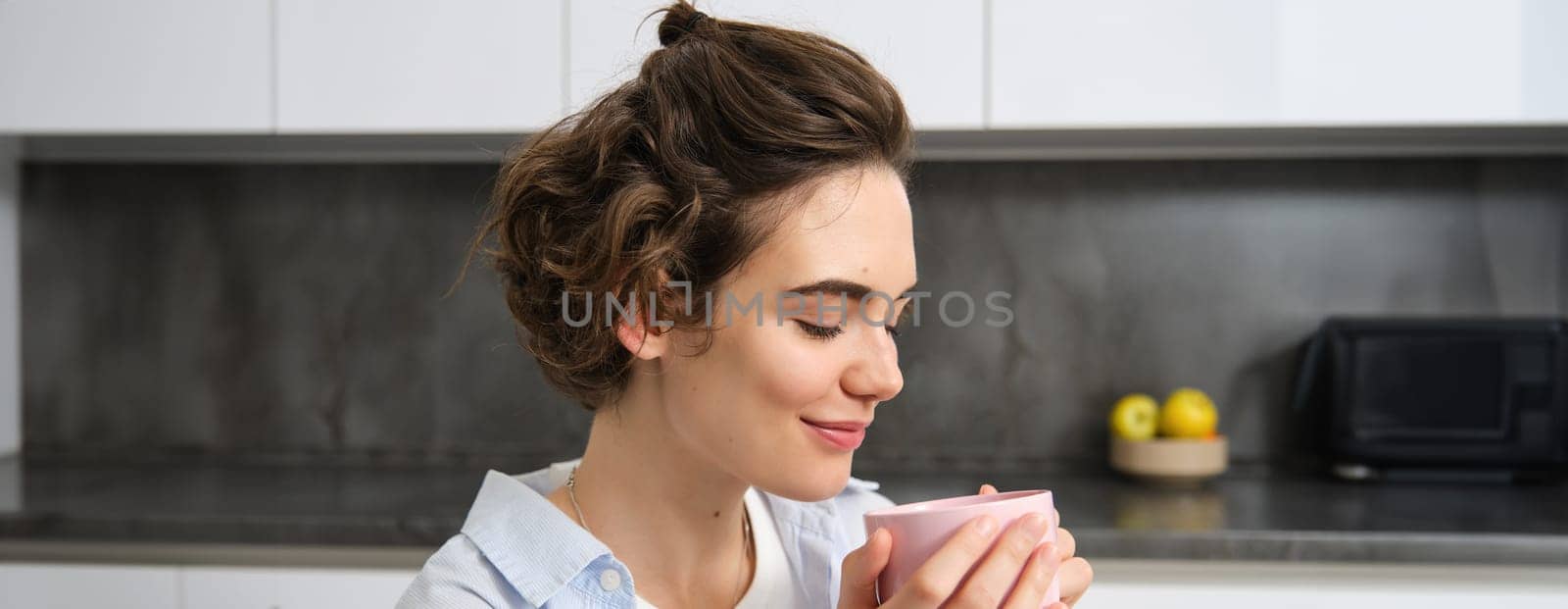 Close up portrait of beautiful woman, drinking coffee at home, looking tender and relaxed, enjoys weekends indoors, enjoys spending time alone by Benzoix