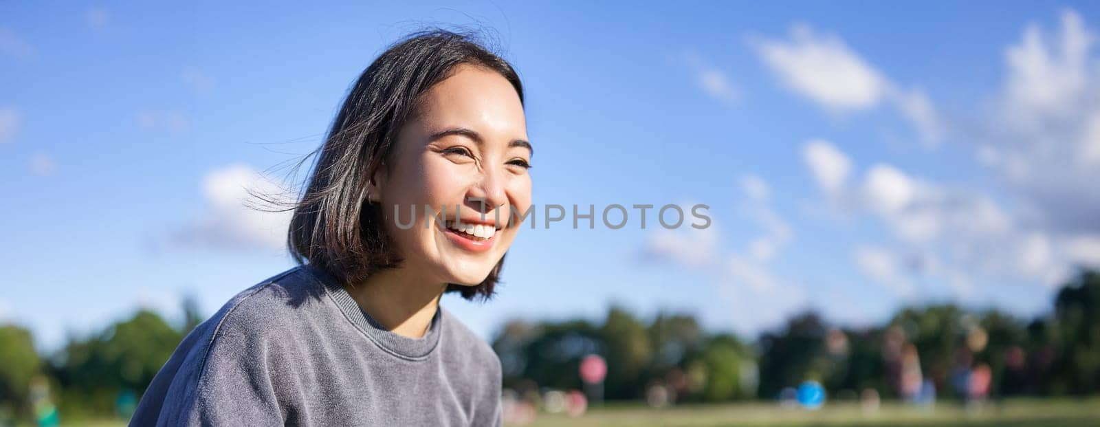Vertical shot of happy korean girl sitting in park, learning how to play ukulele, singing and relaxing.