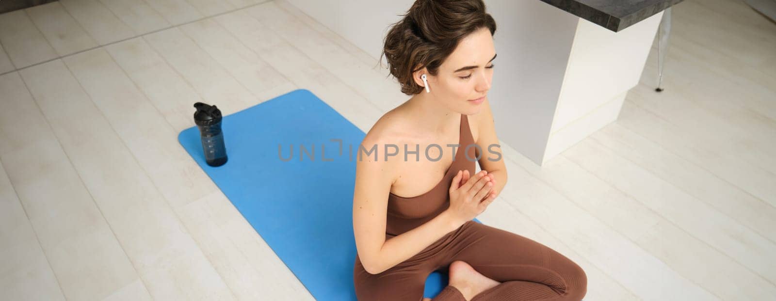Mindfulness and meditation. Young spiritual woman, does yoga, sits in meditation pose in headphones, with workout application, training guide in her smartphone.