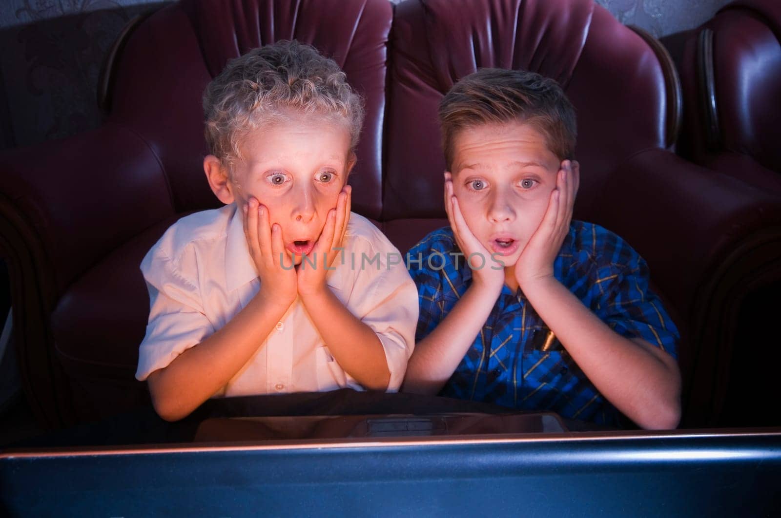 Frontal view of two brothers aged 7 and 13 in the darkened room shocked looking at the TV