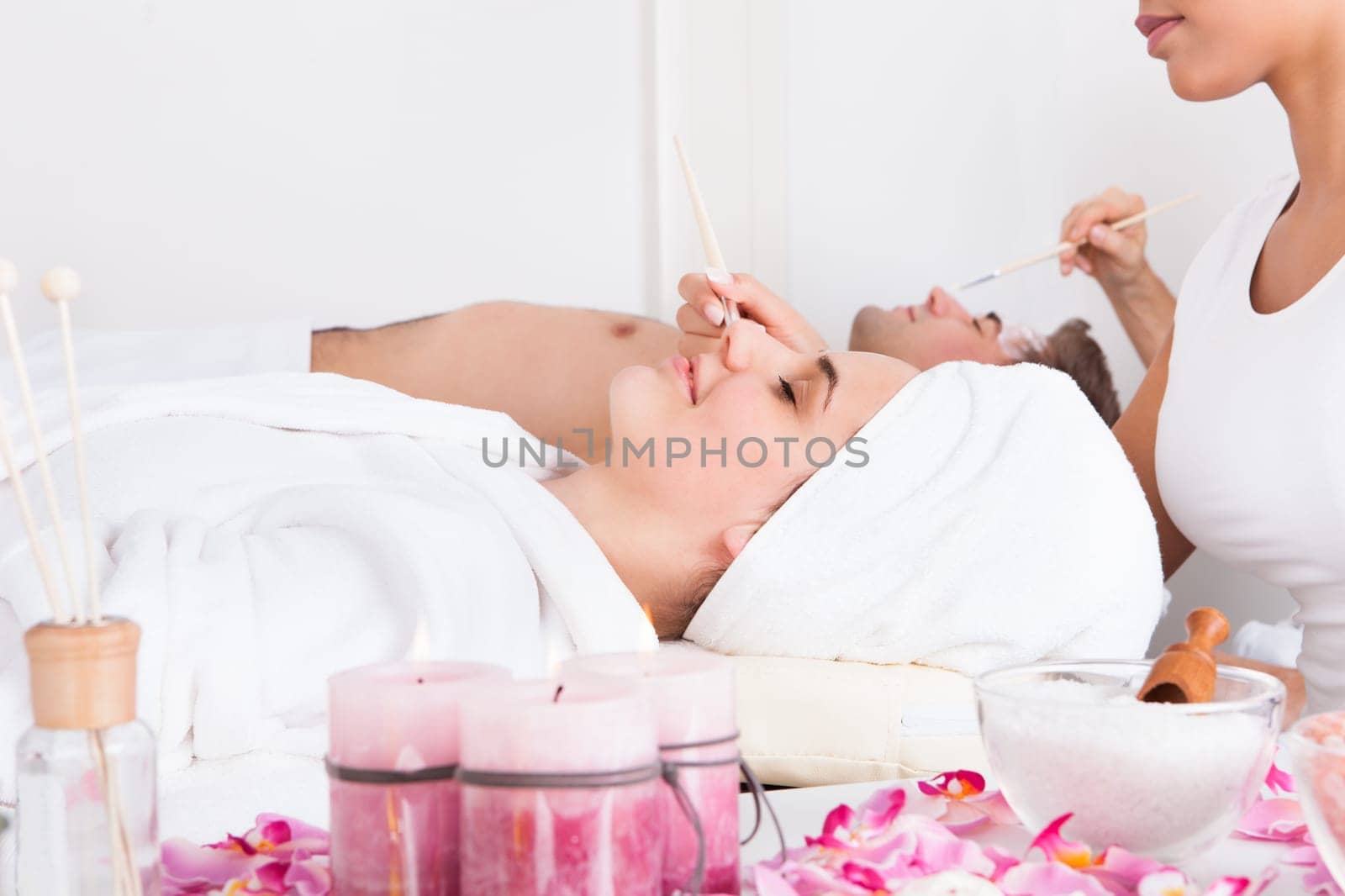 Therapist Applying Facial Mask To Young Couple At Beauty Salon