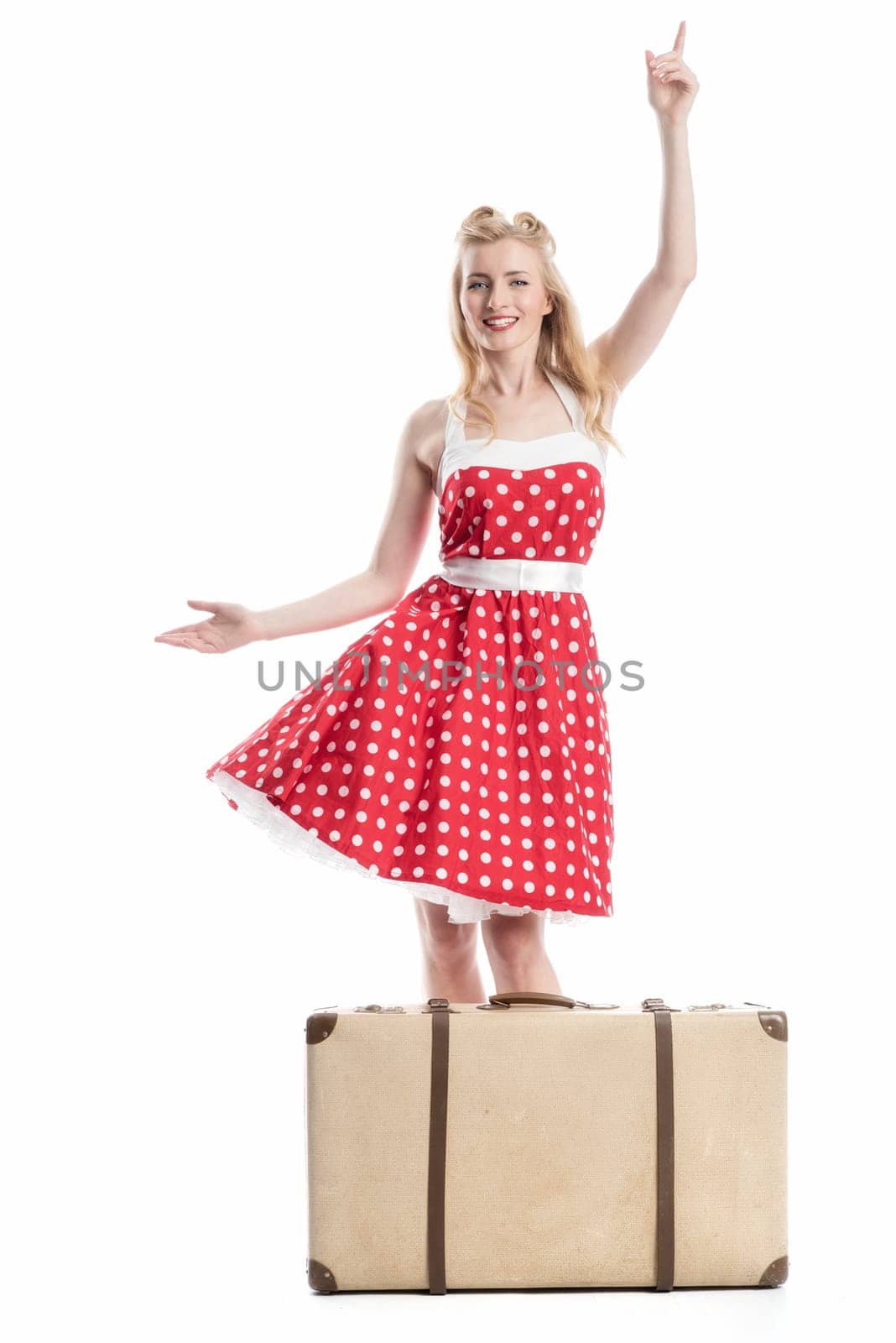 a woman in rockabilly style stands behind a suitcase and points up