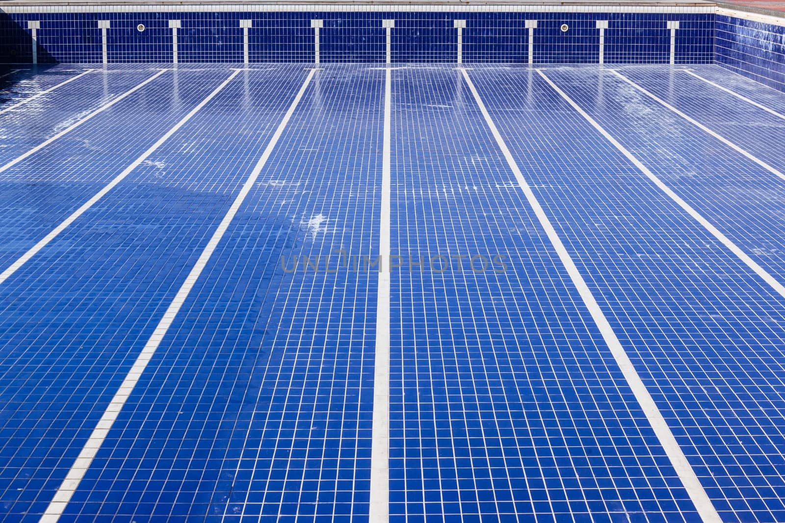 Swimming pool with blue ties and swim lane tile markings empty of water for maintenance