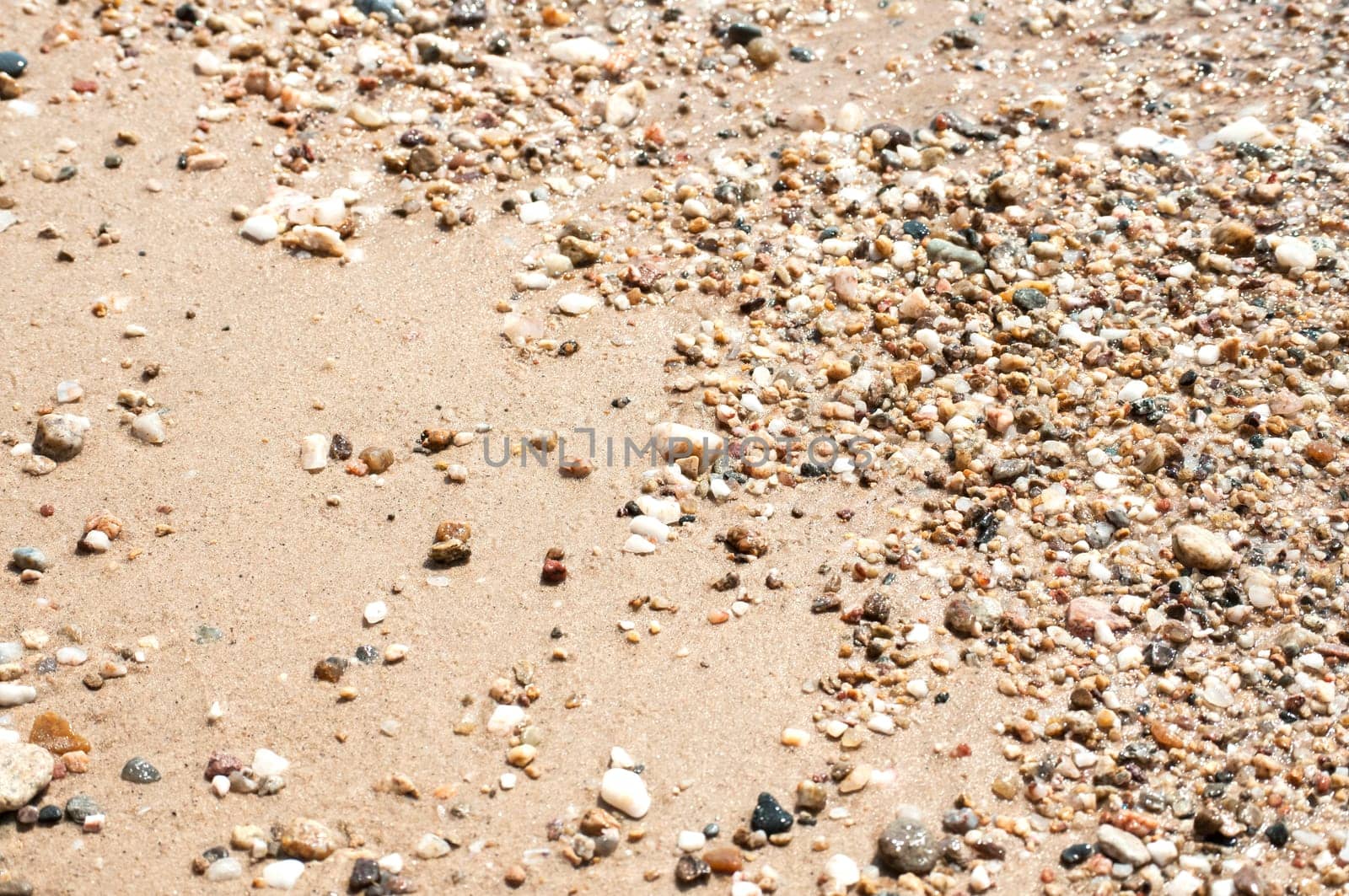 Small pebbles on sand beach closeup wetted by sea water as backgound