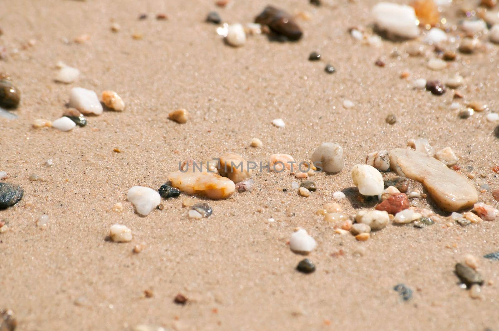 Small pebbles on sand beach closeup wetted by sea water as backgound