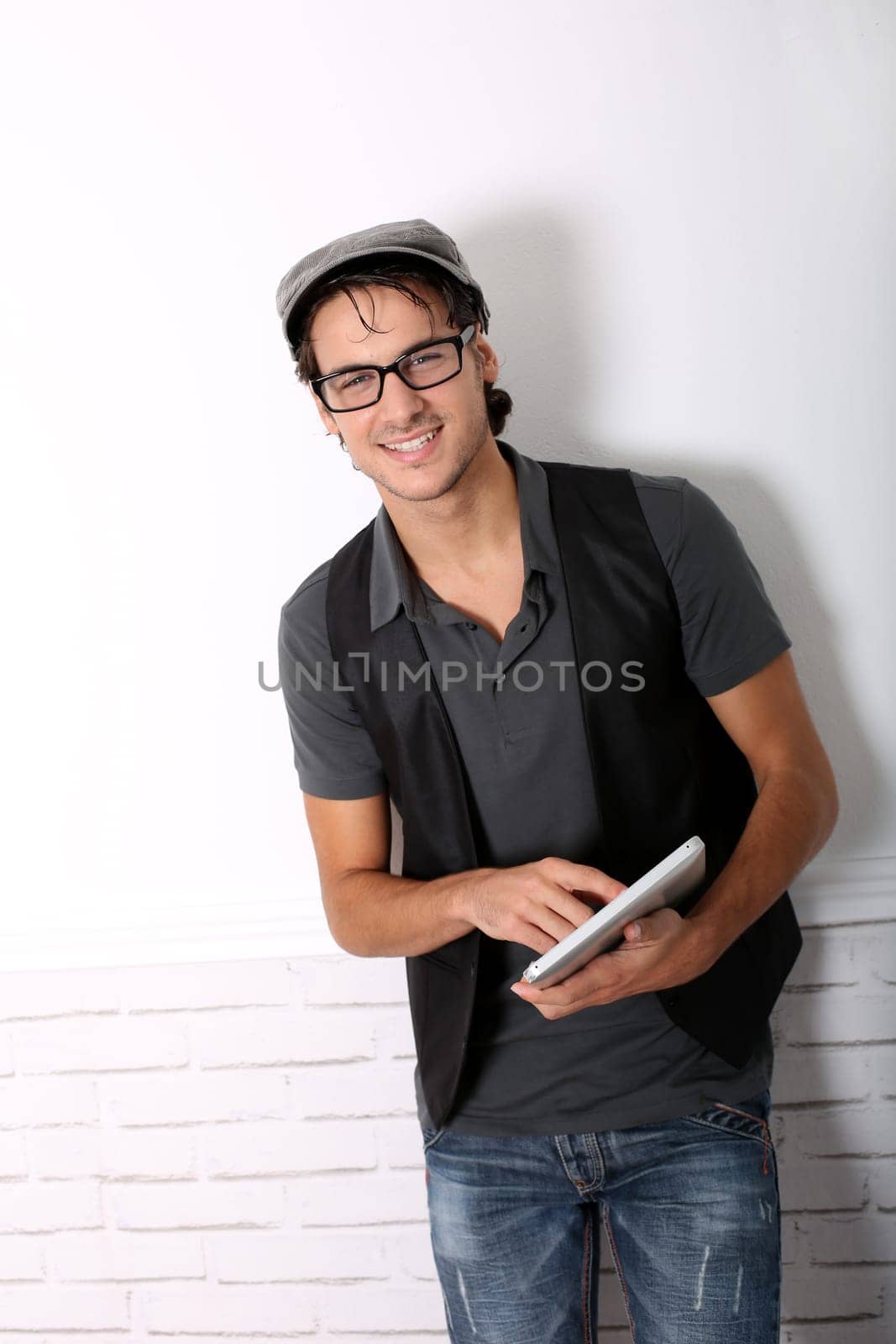 Trendy guy using electronic tablet leaning on wall