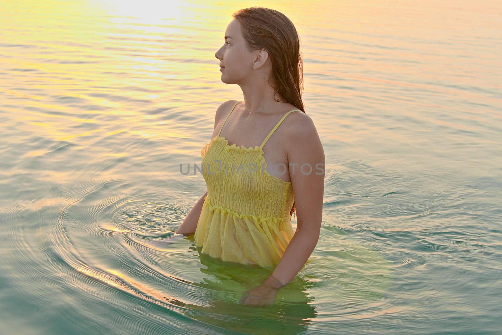 Beautiful woman relaxing on the beach in the morning after swimming against the backdrop of sunrise in the ocean.