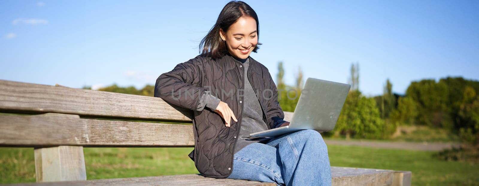 Portrait of smiling woman sitting with laptop, working on project or studying remotely, enjoying being in park.