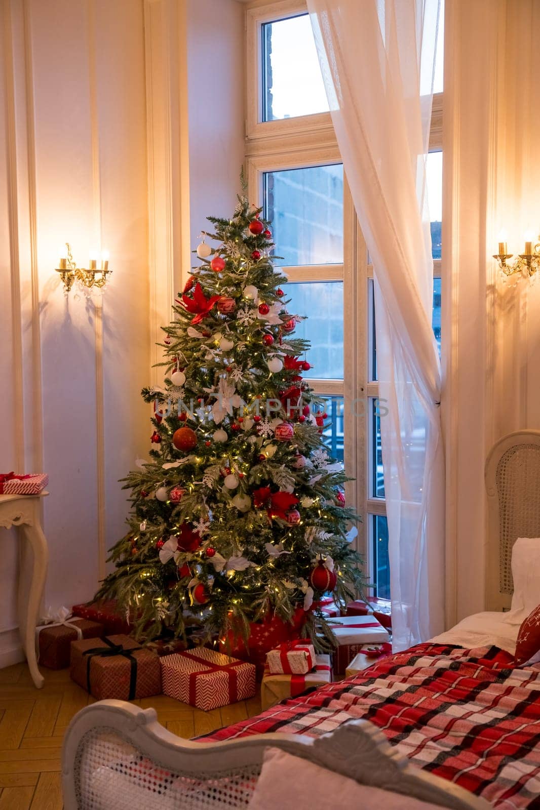 Winter Xmas Hygge home decor. Festive cozy bedroom in Skandinavian style with bed and two snow-covered decorated christmas tree with gifts.